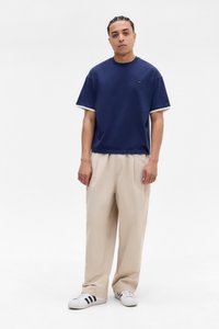 Marineblå kortærmet skjorte med hvide accenter, beige bukser og sneakers med sorte striber. Simpelt design, afslappet pasform, bomuldsmateriale.