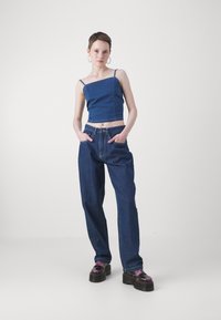 Denim kratki top s tankim trakama, uparen s širokim plavim trapericama i debelim crnim platformama s ljubičastim akcentima.
