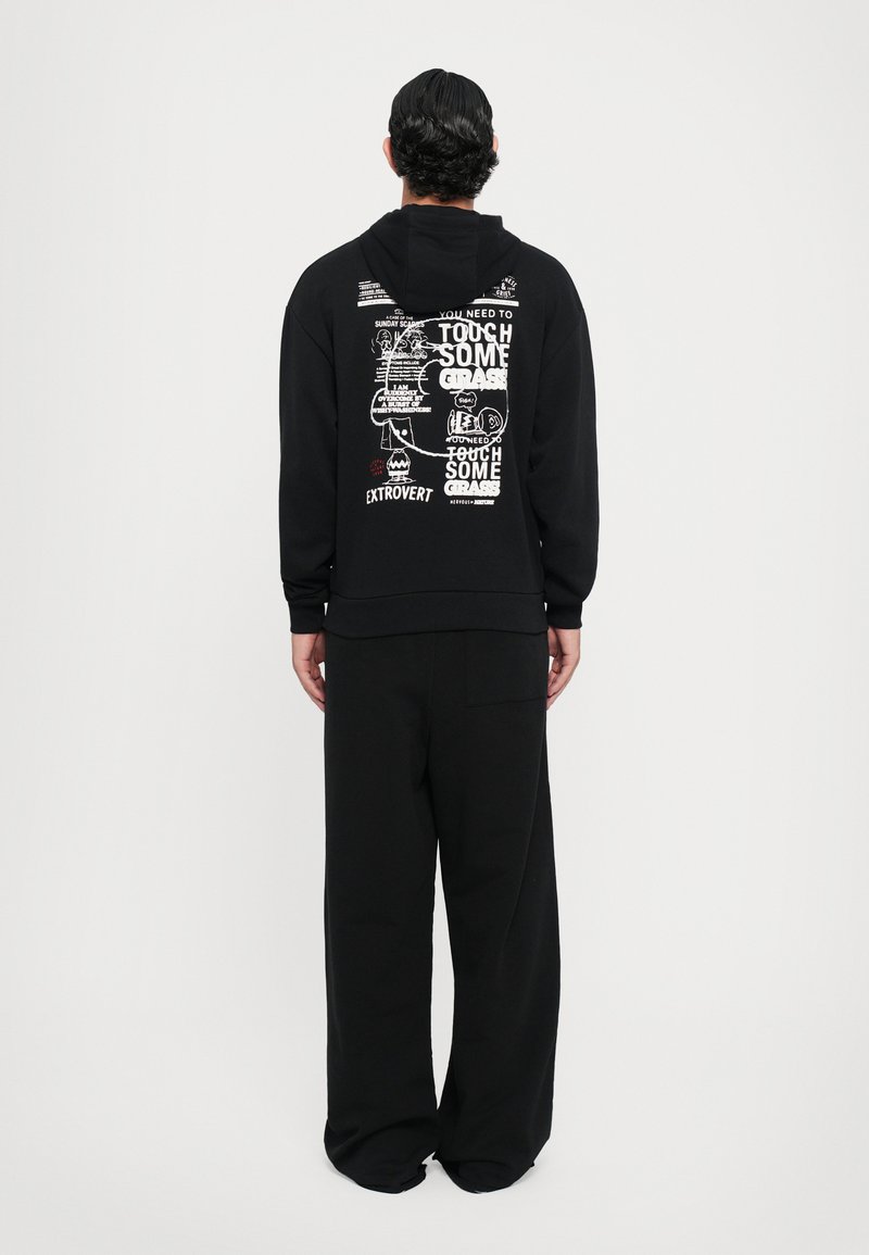 Haut à capuche noir avec une grande imprimé graphique en blanc et rouge au dos. Présente une coupe décontractée et des manches longues, associé à un pantalon noir ample.