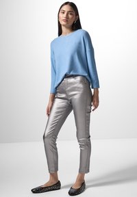 Blå, oversized tröja med rundad halsringning, matchad med glänsande silverfärgade tighta byxor och svarta ballerina-skor med metalldekorationer.