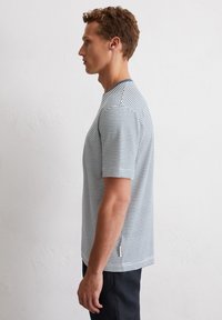 T-shirt rayé à manches courtes, fabriqué en tissu léger. Présente des rayures horizontales bleues et blanches, un décolleté arrondi et une fente sur le côté.