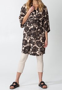 Blommig kimono i beige med svarta pionmönster, åtdragen i midjan. Kombinerad med ljusbeige cropped-byxor och svarta sandaler.