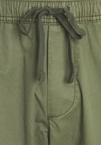 Olijfgroene broek met elastische tailleband en een zichtbaar getailleerd stoffen koord, met een voorzak en gedetailleerde stiksels.