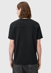 Camiseta negra de manga corta con un acabado texturizado, cuello redondeado y dobladillo recto. Presenta una parte trasera suave con un sutil detalle de costura.