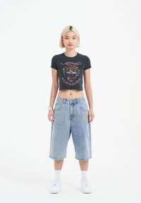 Zkrácené černé tričko s grafikou tygra a textem "Los Angeles"; džíny šortky v světle modré, ke kolenům, s kapsami a detaily šití.