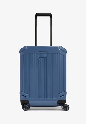 Maleta rígida azul con asa extensible y cuatro ruedas giratorias, vista frontal con estrías verticales y etiqueta de la marca cerca del centro superior.