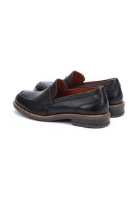 Mocassins en cuir noir avec une finition lisse, une pointe arrondie, des coutures contrastantes et une semelle légèrement empilée en brun. Aucun logo visible.