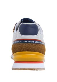 Baskets blanches avec un talon marine et des accents en daim marron. Présentent une semelle jaune avec une bande rouge, des matériaux texturés et un motif de texte répété.