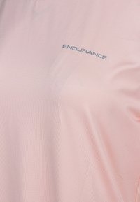 Ljusrosa träningsskjorta gjord av ett mjukt, andningsbart material, med ordet "ENDURANCE" tryckt i grått över bröstpartiet.