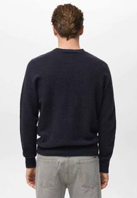 Temno modri pleteni pulover z dolgimi rokavi, okroglo izreza in rebrastimi manšetami ter robom, nosi se z svetlo sivo hlačami. Mehka tekstura, brez vidnih vzorcev.