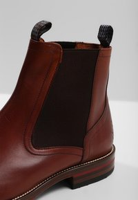 Bottine en cuir marron avec panneau élastique et languette texturée, dotée d'une semelle surpiquée et d'une semelle multicouche aux couleurs variées.