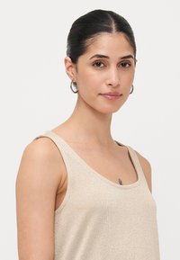 Beige kimaltuva tanktoppi, jossa on pyöreä pääntie ja leveät olkaimet, jossa on pehmeä, teksturoitu kangas, joka vangitsee valon.