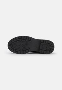 Suela de zapato de goma negra con surcos profundos, con un diseño en patrón para mayor tracción. Punta redondeada y plana, y una construcción gruesa y duradera.
