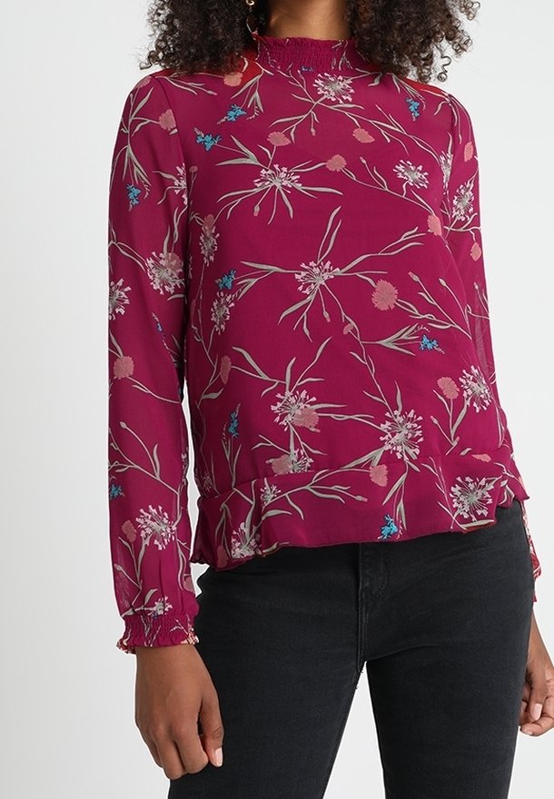 Mauve blommig blus med långa ärmar, smockad halsringning och veckade manschetter. Har flerfärgade blommönster på ett mjukt tyg.