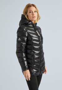 Juodas pūkinis švarkas su blizgiu paviršiumi, užtrauktuku priekyje, gaubtu ir šoninėmis kišenėmis. Yra logotipas ir siuvinėjimo raštas visame švarke.