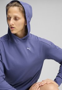 Hanorac cu glugă de culoare mov, cu o textură netedă și un design ajustat. Oferă un mic logo alb pe piept și un guler relaxat.