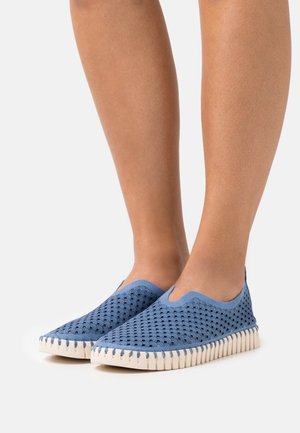 Blue slip-on shoes featuring a perforated upper, textured detailing, and a cream-colored rubber sole with zigzag accents.