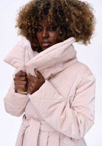 Lichtroze gewatteerde pufferjas met een oversized kraag en riemsluiting. Heeft een glanzende textuur en ruitvormige stiksel.