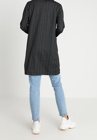 Long manteau noir à rayures grises fines, coupe décontractée, assorti à un jean skinny bleu clair et des baskets blanches.