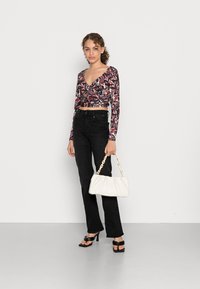 Camisola de mangas longas com decote V profundo e padrão abstrato em vermelho e branco, combinada com jeans pretos de cintura alta e boca de sino, e uma bolsa branca com alça de corrente.
