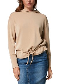 Beige huvtröja med långa ärmar och cinchat midja. Mjuk tyg med dragsko vid fållen. Bärs tillsammans med en denimkjol.