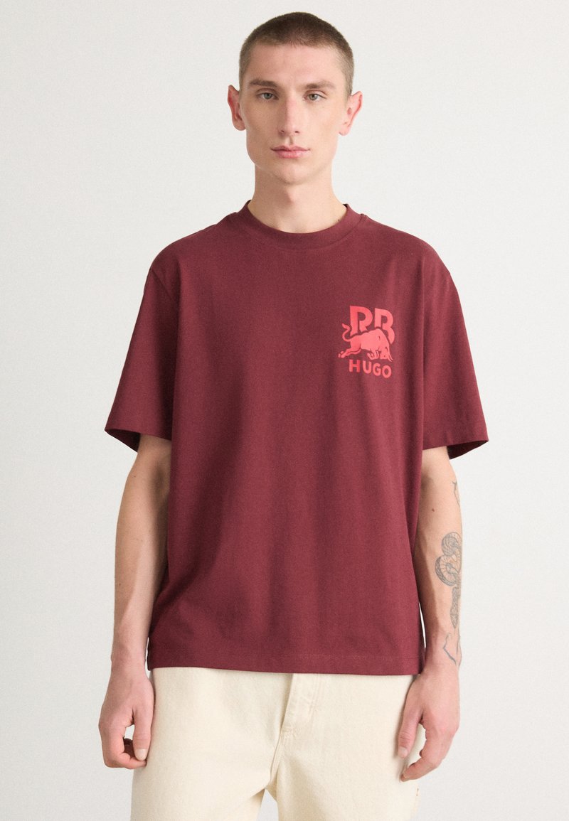 Burgundy cotton t-shirt with short sleeves. Features a light red graphic logo on the left chest. Relaxed fit and crew neck design.