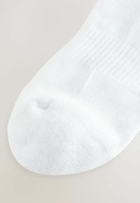 Fehér pamut zokni sima textúrával, bordás bokarésszel és lekerekített orral. Nincsenek látható minták vagy további díszítések.