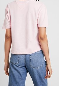 Camiseta corta rosa de algodón suave con mangas cortas, que presenta un escote en V y un diseño liso. Combinada con jeans de color azul claro.