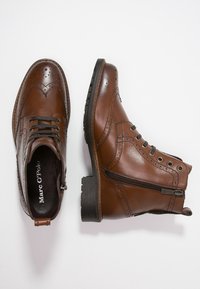 Brune læder ankelstøvler med vinge-design, der har snørebånd og lynlås i siden. Textureret overflade og kraftig gummisål. Brand: Marc O'Polo.