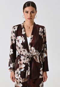Bloemen kimono jas in donkerbruin, met een wikkelontwerp, lange mouwen en een riem. Gemaakt van zachte stof met grote crèmekleurige en roze bloemen.