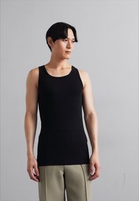 Musternöörne must tank top, pehme kangaga. Omab ümarat kaelust ja pole nähtavaid õmblusi, kantud heledate pükstega.