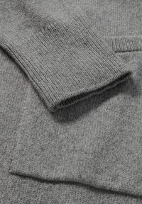 Grauer Strickpullover mit gerippten Bündchen und Struktur. Nahaufnahme zeigt den weichen Wollstoff mit subtilen Farbvariationen.