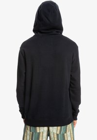 Sudadera negra con una gran capucha, bordes sin terminar y puños acanalados. Diseño sencillo sin logotipos ni patrones visibles en la parte posterior.