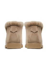 Beige suède enkellaarsjes met een zachte bontvoering aan de bovenkant, met een subtiele naaddetail op de hak en een platte tan rubberen zool.