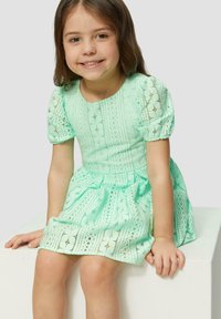 Robe vert menthe clair avec manches bouffantes, détails en dentelle et jupe plissée. Fabriquée en tissu respirant avec des motifs complexes.