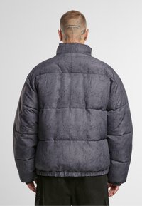 Puffjacka i mörkgrått med en kviltad design, hög krage och textil med en matt finish. Gummibeklädda ärmslut och nederkant.
