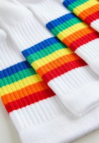 Dažādkrāsu zeķes ar horizontālām svītrām sarkans, oranžs, dzeltens, zaļš un zils, uz balta fona un ar ribotu struktūru.