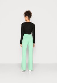 Sweater preto cropped com mangas longas, combinado com calças largas em verde menta de cintura alta, vistas de trás. Ténis brancos e brincos de argola.