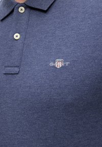 Marineblaues Polohemd mit zwei cremefarbenen Knöpfen und einem kleinen gestickten Schildlogo mit drei Sternen und Streifen auf der Brust.
