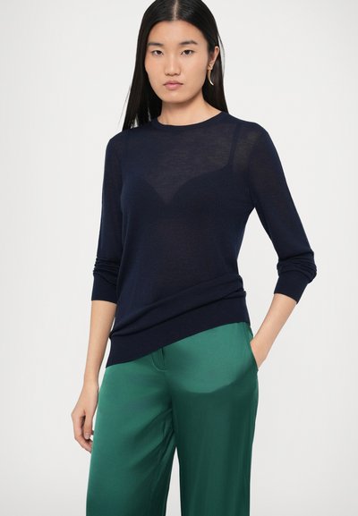 Tumesinist läbipaistvast vimkudega kampsun ümar kaelusega ja kolmveerandvarrukatega. Ühitatud roheliste satiinpükstega, millel on küljetaskud.