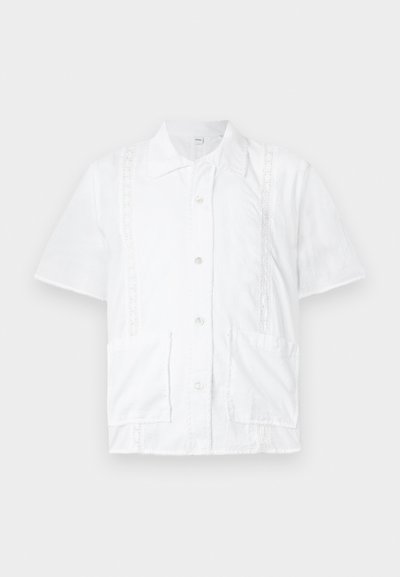 Weißes Kurzarmhemd mit kragenförmigem Halsauschnitt, zwei Fronttaschen, Spitzenbesatz und Knöpfen in der Mitte. Aus Baumwollmaterial.