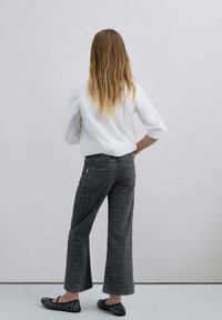 Los vaqueros negros de pierna ancha presentan un patrón texturizado, una cintura alta y dos bolsillos traseros. Combinados con una camisa blanca de botones y unas bailarinas negras.
