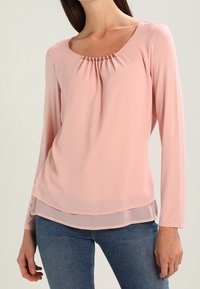 Jasnoróżowa bluzka z długim rękawem, z kwadratowym dekoltem, fałdami i dekoracyjnym haftem, warstwowym dołem oraz miękką, gładką teksturą materiału.