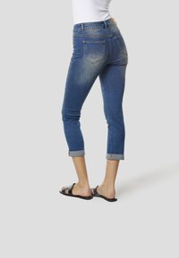 Dunkelblaue Jeans aus Denim mit schmal zulaufendem Schnitt, umgeschlagenen Säumen und einem verblassten Finish. Auf der Rückseite befinden sich zwei gestickte Taschen und dezente Details.