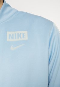 Felpa Nike azzurro chiaro con collo alto, tessuto strutturato e loghi bianchi a contrasto sul petto.