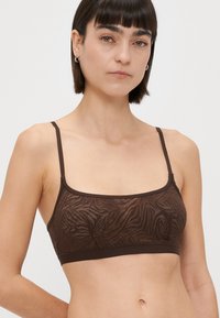 Rjav modrček z rahlo prosojno tkanino in subtilnim zebrovim vzorcem. Tanke naramnice in gladek pas na dnu ponujata minimalistični dizajn.