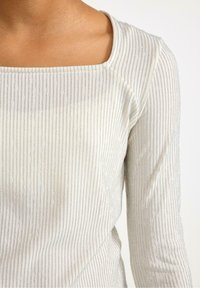 Lysfarvet, ribbet top med firkantet udskæring og lange ærmer, der har en subtil glans og sølvfarvede vandrette striber.