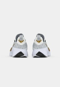 Pair of gray and white athletic shoes with gold swoosh, textured heel, and black triangular tread, viewed from the back on white background.