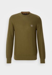 Pull olive en maille côtelée, col rond et manches longues. Présente un petit logo brodé sur la poitrine gauche.