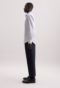 Camicia button-up azzurro chiaro con un piccolo motivo floreale, abbinata a pantaloni navy scuri e scarpe stringate nere, vista di lato.